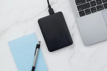 An external hard drive next to a laptop on a white marble desk