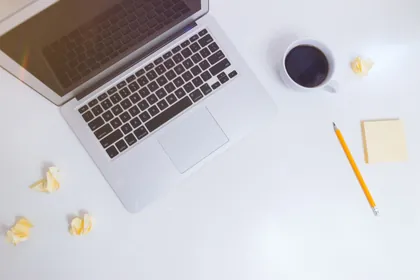 An open laptop and a cup of coffee on a white desk, seen from above